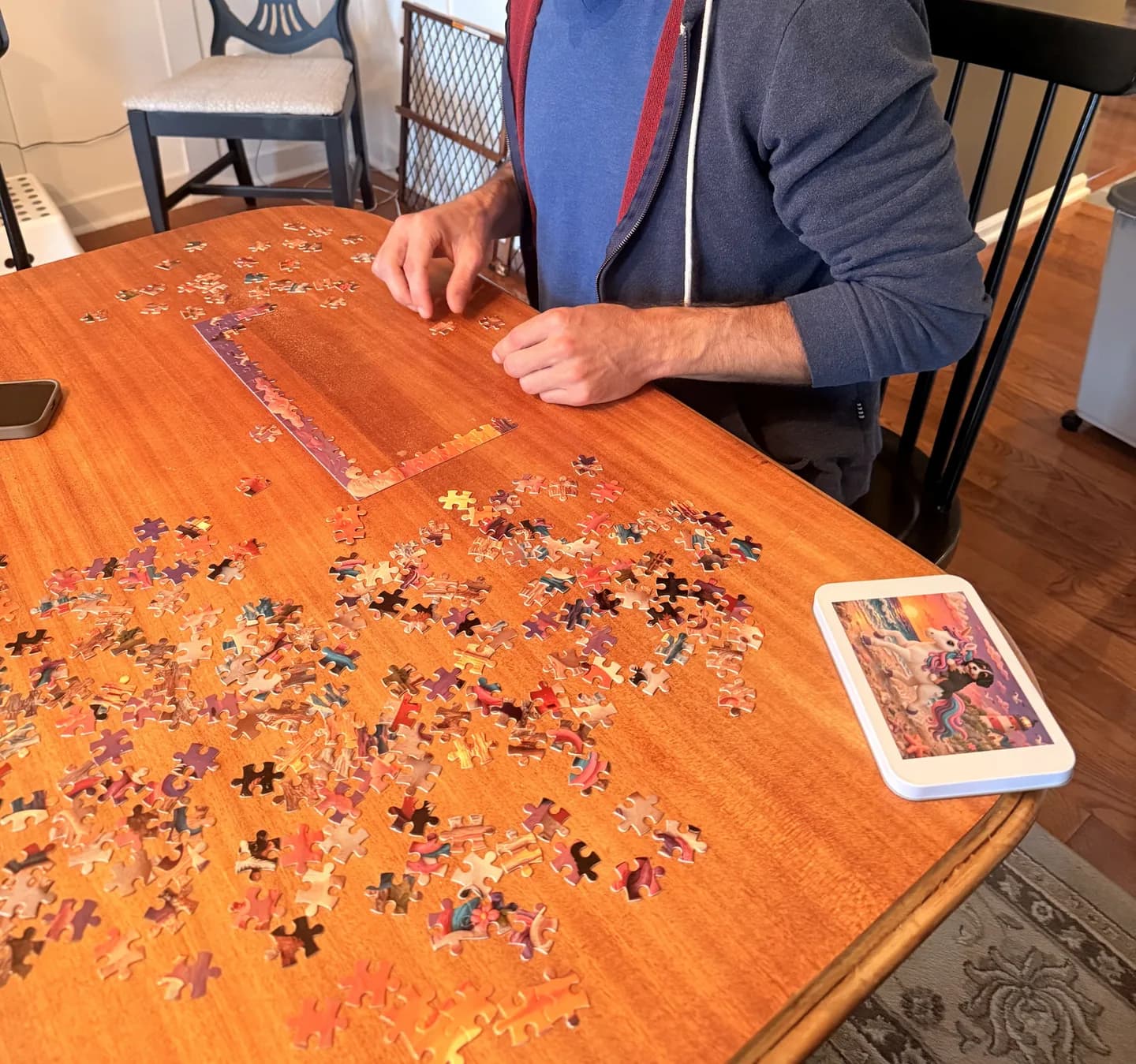 Person assembling puzzle pieces on a wooden table beside a tin printed with the clay-style unicorn-and-puppy artwork