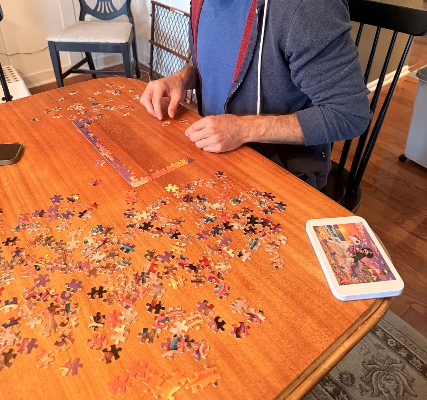 A person assembling puzzle pieces on a wooden table beside a tin printed with the clay-style unicorn and puppy